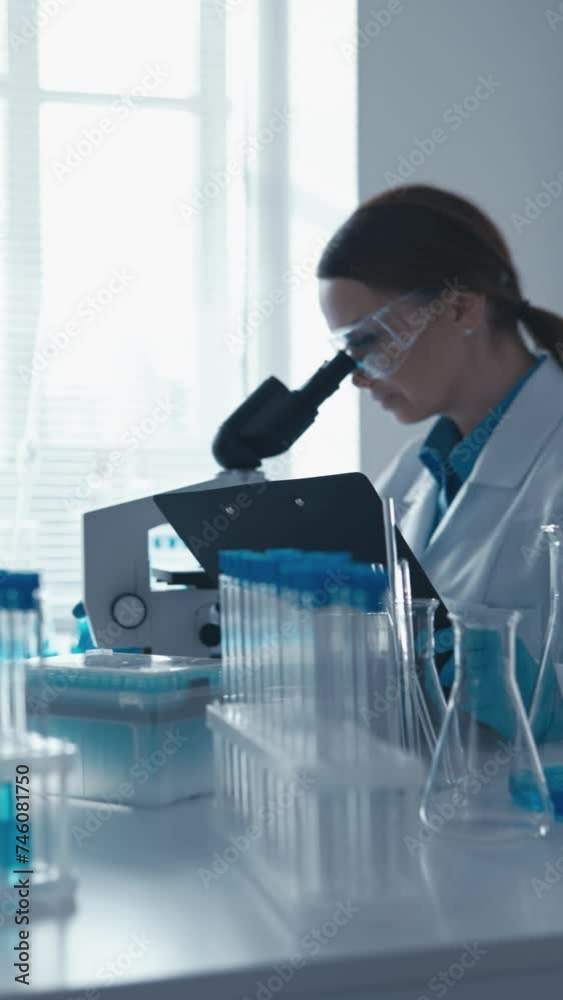 Poster In this vertical video, a scientist in a biology lab focuses on conducting research on genetic modifications using cutting-edge technology. His attentive gaze and working attitude testify to his deep