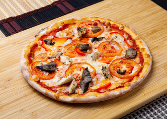 Pizza with mushrooms, tomatoes, cheese and chicken on a wooden board.