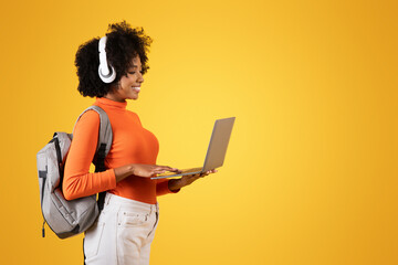 Focused young woman with afro hair and white headphones, using a laptop