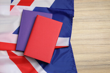 Learning foreign language. Different books and flag of United Kingdom on wooden table, top view with space for text