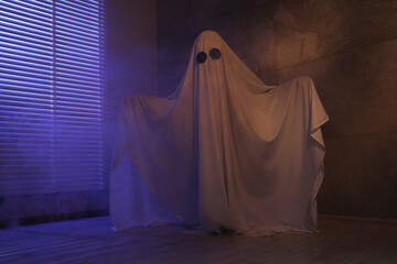 Creepy ghost. Woman covered with sheet near window in color lights