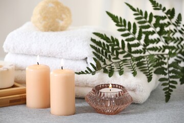 Fototapeta na wymiar Spa composition. Burning candles, towels and loofah on soft grey surface