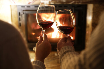 Couple clinking glasses of wine near fireplace at home, closeup