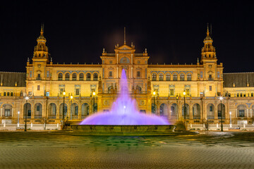 Vista nocturna de la Plaza de España de Sevilla al anochecer, con la fuente central iluminada de...