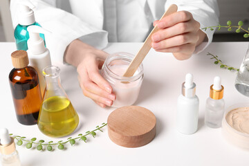 Dermatologist with jar testing cosmetic product at white table indoors, closeup