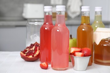 Tasty kombucha in glass bottles, jar and fresh fruits on white tiled table