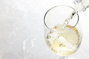 Pouring tasty aromatic wine in glass at gray marble table, closeup. Space for text