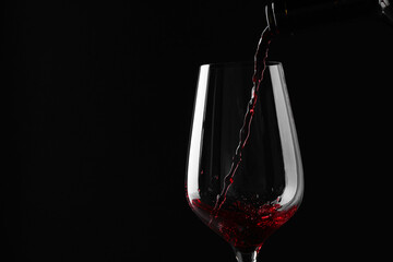 Pouring red wine into glass against black background, closeup. Space for text