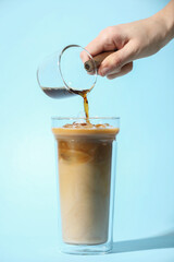Woman making iced coffee on light blue background, closeup