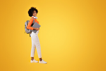 Fototapeta premium Confident young student in a vibrant orange turtleneck and white pants looks back with a smile