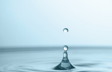 Splash of clear water with drop on light grey background, closeup