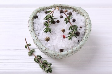 Salt with peppercorns and thyme in bowl on white wooden table, closeup