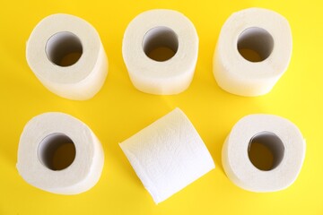 Many soft toilet paper rolls on yellow background, flat lay