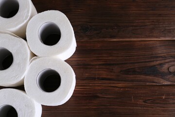 Many soft toilet paper rolls on wooden table, flat lay. Space for text