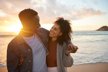 Smiling multiethnic couple standing together on a sandy beach at dusk