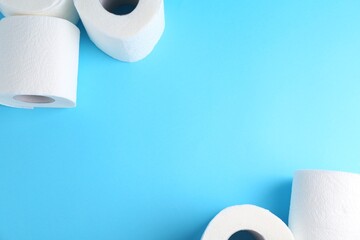 Soft toilet paper rolls on light blue background, flat lay. Space for text