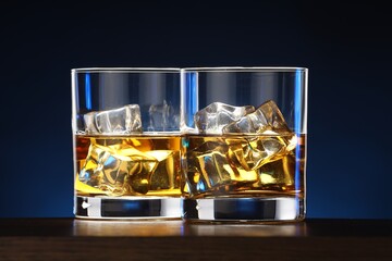 Whiskey with ice cubes in glasses on table, closeup