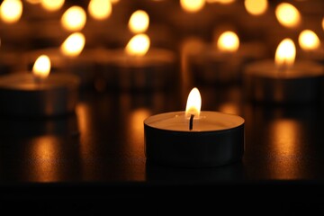 Burning tealight candles on dark surface, closeup