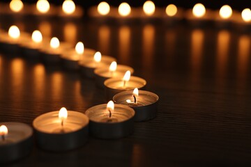 Burning candles on wooden table in darkness, closeup. Space for text