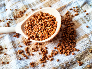 Buckwheat scattered on textured fabric and in a wooden spoon. Grits for cooking. Texture, background, copy space and place for text