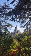 Vertical photograph of the bell tower framed by the branches and all the green vegetation of the park in Rocamadour in France