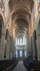 Obraz premium Vertical photograph of the interior of the Rocamadour church in France from the central aisle. The altar has a very high ceiling at the back and there is a man sitting on the chairs.