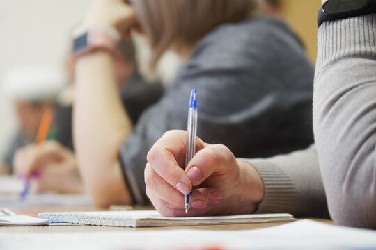 An adult woman with a fountain pen sits next to colleagues and writes in a notebook during a meeting or professional development training session.Photo. No face. Selective focus