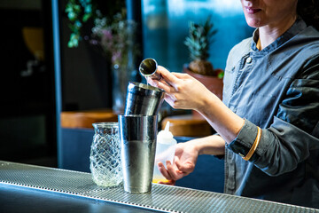 Fototapeta na wymiar barman prepara un cocktail de piña colada con hoja de piña en un vaso decorado sobre la barra de un cocktail bar exclusivo por la noche en ambiente de fiesta, camarera close up