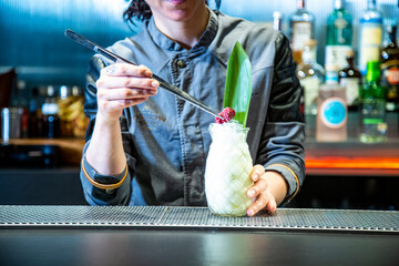 barman prepara un cocktail de piña colada con hoja de piña en un vaso decorado sobre la barra de...