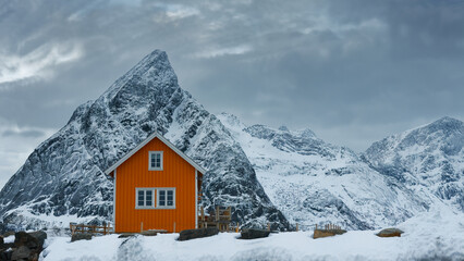 Cloudy winter landscape with snowy mountains in the background and a cabin house in the foreground....