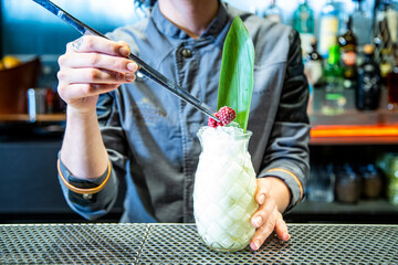 barman prepara un cocktail de piña colada con hoja de piña en un vaso decorado sobre la barra de...