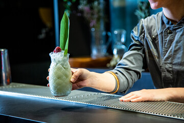 barman prepara un cocktail de piña colada con hoja de piña en un vaso decorado sobre la barra de un cocktail bar exclusivo por la noche en ambiente de fiesta, camarera close up