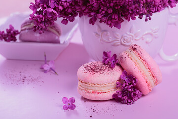 Obraz na płótnie Canvas Close up of Pastel colored sweet french macaroons with lilac flowers on pink background. Beautiful composition for bakery and pastry shop