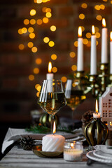 Luxury elegant Christmas dinner table setting with old vintage golden chandelier, candles, fir tree branches, wooden furniture. Porcelain houses as centrepiece, garland with lights on background