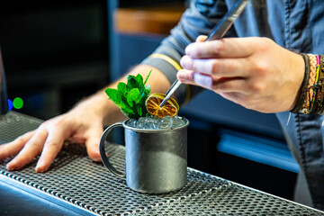 Barman prepara un mojito cocktail en la barra de un cocktail bar exclusivo vestido con una chaquetilla azul con iluminación nocturna, detalle close up