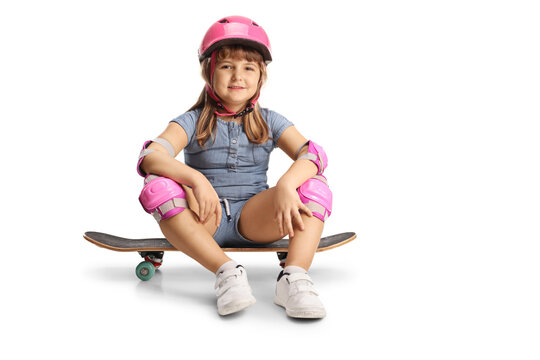 Full length profile shot of a little girl sitting on a skateboard, wearing elbow, knee pads and helmet