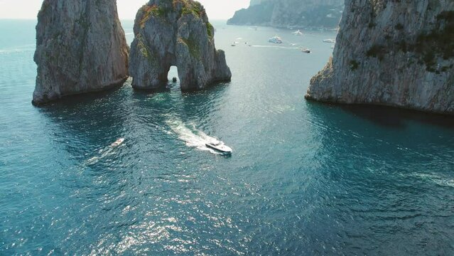 Capri Island with Faraglioni cliffs against a backdrop of a bustling sea. Speedboats cut through the water, leaving trails of white foam in their wake.