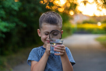 A child looks at the water through a magnifying glass against the background of nature