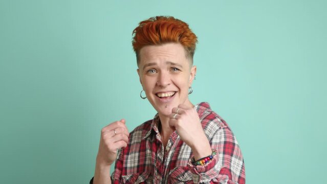 A cheerful lesbian with a modern hairstyle playfully mimics boxing gestures, showcasing her energetic and joyful spirit against a calm teal backdrop. Camera 8K RAW. 