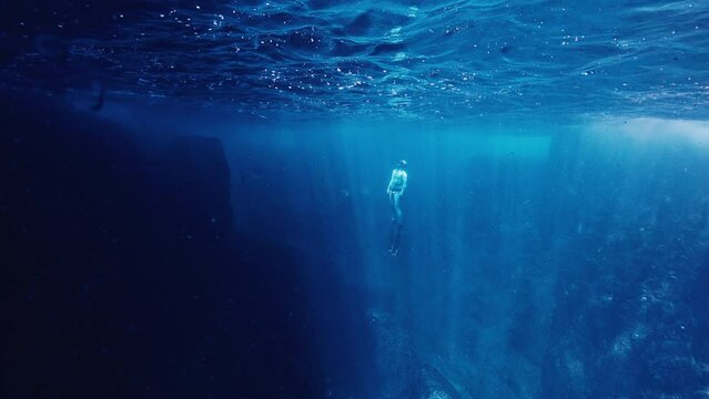 Freediver swims underwater in the sea and ascends near the rock
