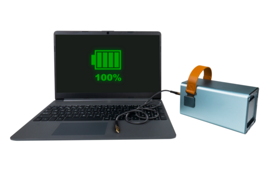 A laptop next to a large power bank (charging station) with a USB cable on a transparent background. On the laptop screen there is a green indicator of 100% battery charge (full charge)