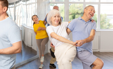 Enthusiastic senior couple, woman and man in sportswear, participating in group class for aged...