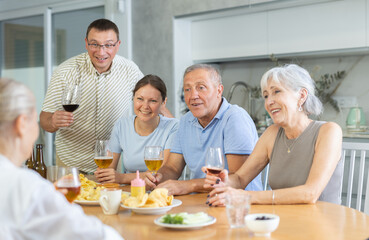 Happy elderly people speaking to each other with enthusiasm while drinking and eating in the kitchen