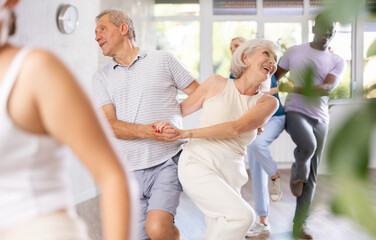 Positive aged man and woman dancing energetic upbeat jive as couple during group training in dance studio - obrazy, fototapety, plakaty