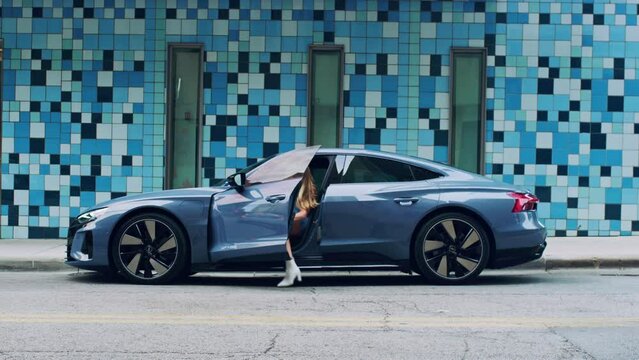 Blonde woman gets into a luxury sports car on a blue tile background