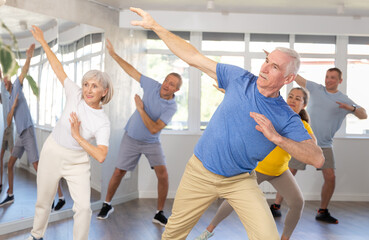 Fototapeta na wymiar Enthusiastic elderly man attending group choreography class, learning modern dynamic dances. Concept of active lifestyle of older generation ..
