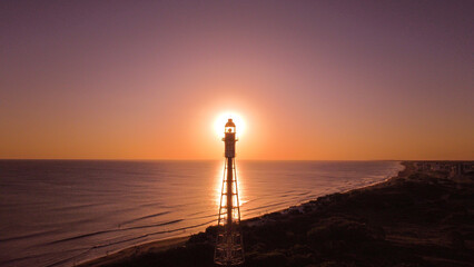 Lighthouse and sun in the background, with people's shadows cast over the top, creating a beautiful orange and blue reflection over the sea.
