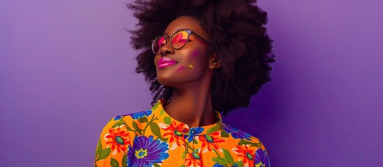 A young woman with glasses and a colorful shirt stands smiling against a violet backdrop in a...