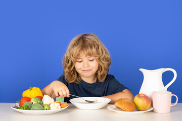 Kid eating soup. Children eat breakfast. Cute child eating lunch soup. Closeup face of kid eating organic food, yogurt, milk. Child healthy eat. Smiling little boy eating food on kitchen.