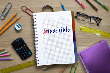 From impossible to possible. Handwriting on notepad on background of desktop with office and school stationery. Word impossible changes to possible. Motivation, setting goals concept.